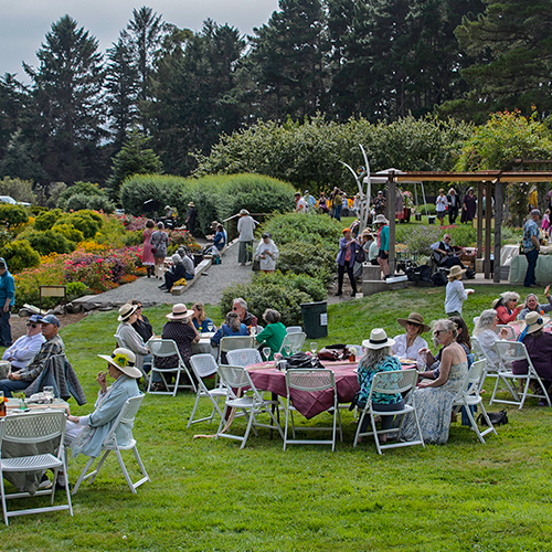 A group of people enjoying a Garden Gala, seated at tables in a vibrant park setting.