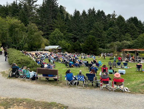 Large crowd gathered on the lawn at Humboldt Botanical Garden for the Annual Summer Music Series, enjoying live music surrounded by scenic greenery.